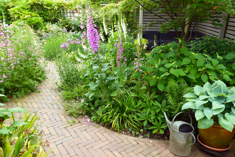 Réalisation d'un petit jardin arrière champêtre l'été avec une exposition partiellement ombragée et des pavés en brique.