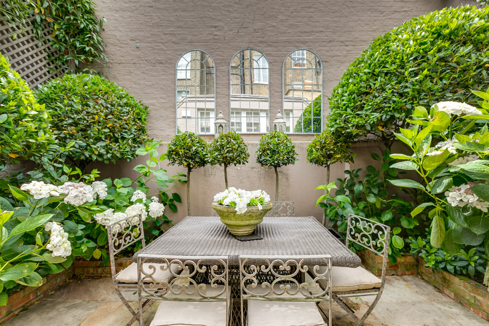 Imagen de jardín romántico en patio con macetero elevado y adoquines de piedra natural
