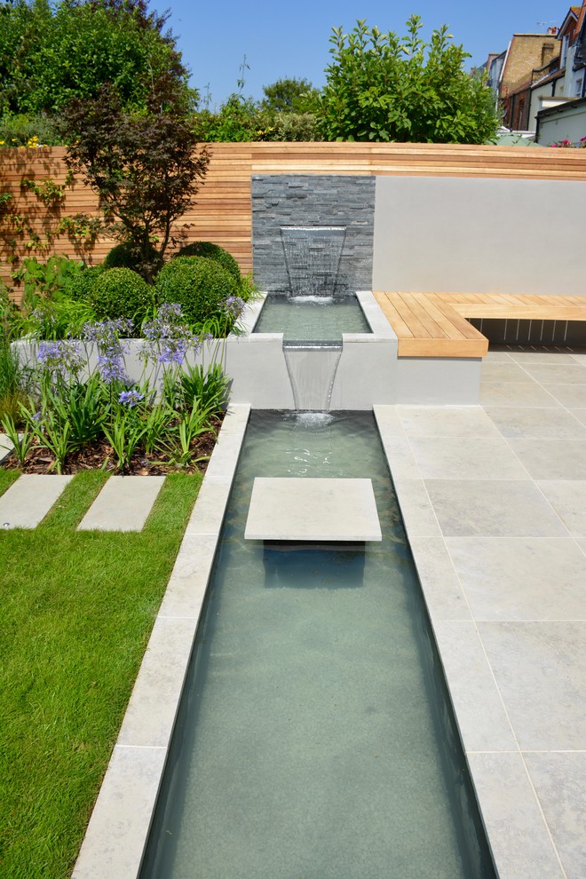 Inspiration for a medium sized contemporary back full sun raised pond for summer in London with natural stone paving.