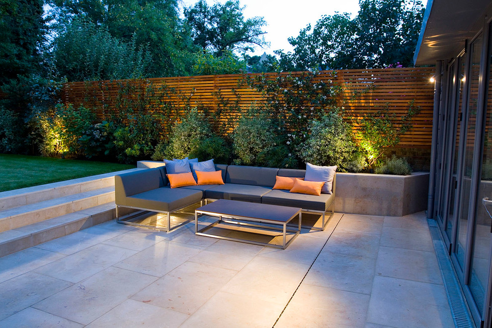 Medium sized contemporary back patio in London with natural stone paving.