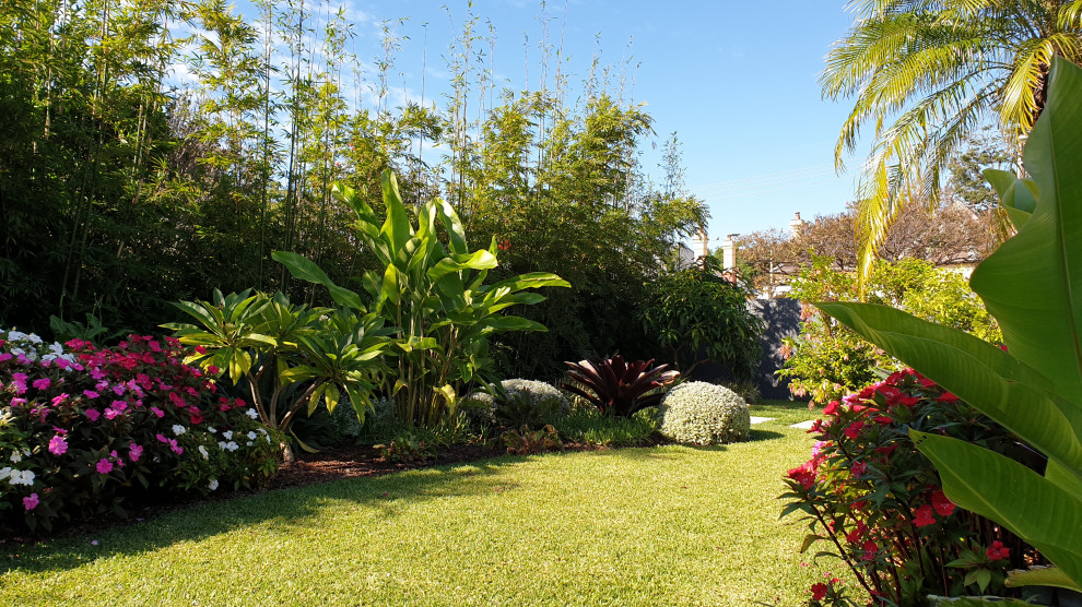 Foto di un giardino tropicale esposto in pieno sole dietro casa con pavimentazioni in pietra naturale