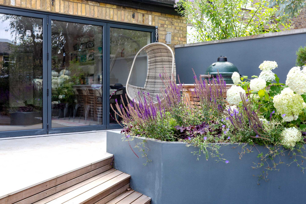 Inspiration for a small contemporary back garden in London with a raised bed and natural stone paving.