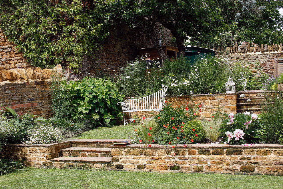 This is an example of a medium sized country back full sun garden for summer in Hertfordshire with a retaining wall and natural stone paving.