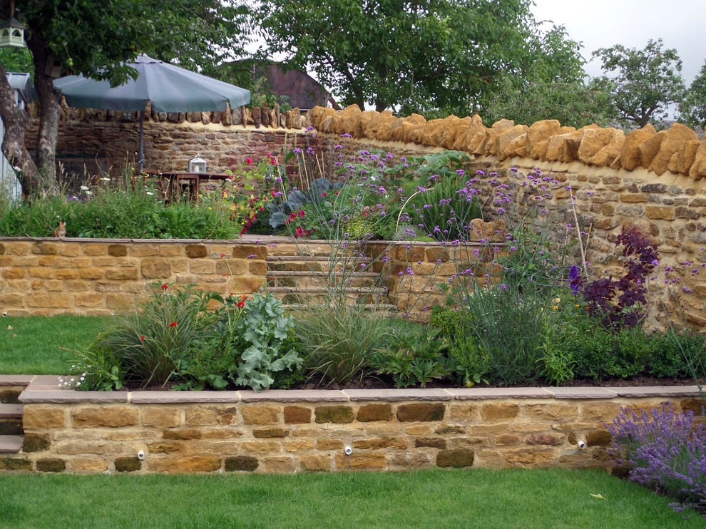 Design ideas for a medium sized traditional sloped full sun garden for summer in Hertfordshire with a retaining wall and natural stone paving.