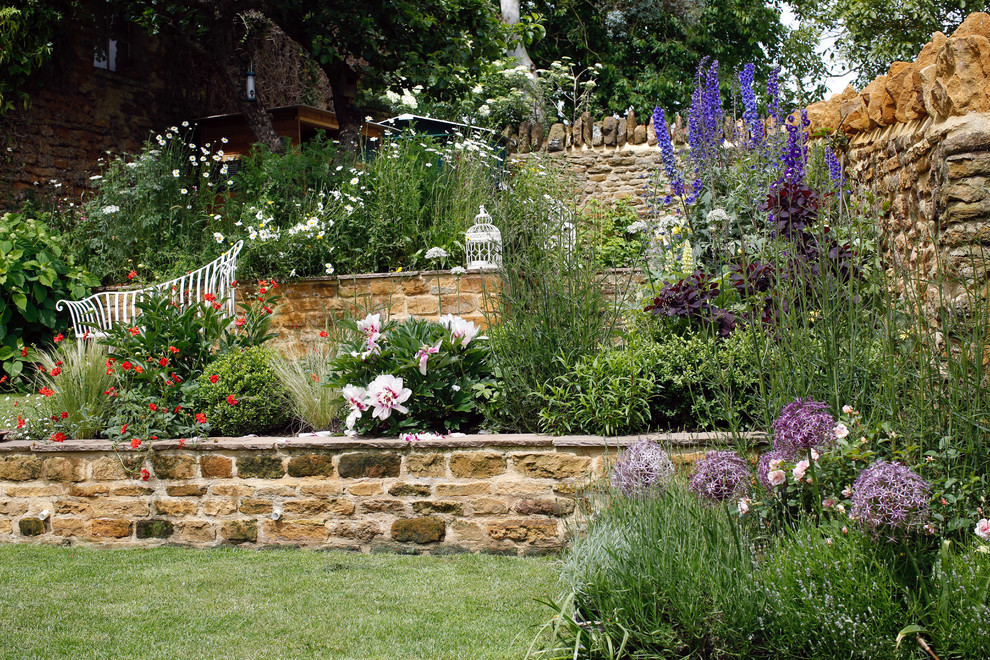 Aménagement d'un jardin arrière campagne de taille moyenne et l'été avec un mur de soutènement, une exposition ensoleillée et des pavés en pierre naturelle.