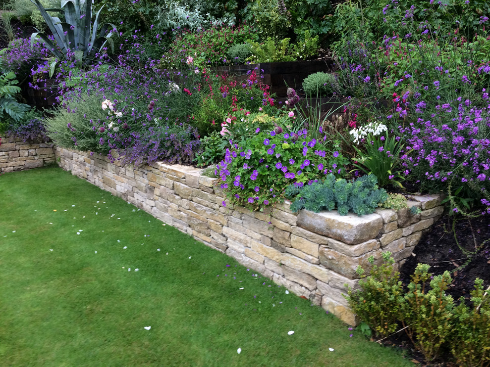 Пример оригинального дизайна: большой весенний регулярный сад на склоне в классическом стиле с подпорной стенкой, полуденной тенью и покрытием из каменной брусчатки
