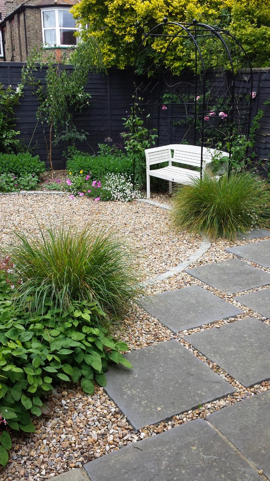 This is an example of a small classic back formal partial sun garden for summer in London with a garden path and natural stone paving.