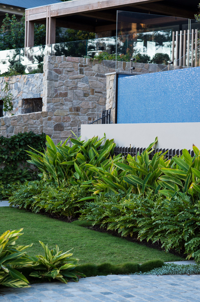 Imagen de jardín tropical grande en primavera en patio delantero con exposición total al sol y adoquines de piedra natural