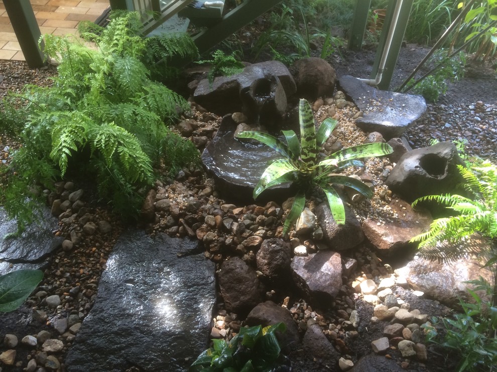 Small rustic back fully shaded garden in Sunshine Coast with a water feature and natural stone paving.