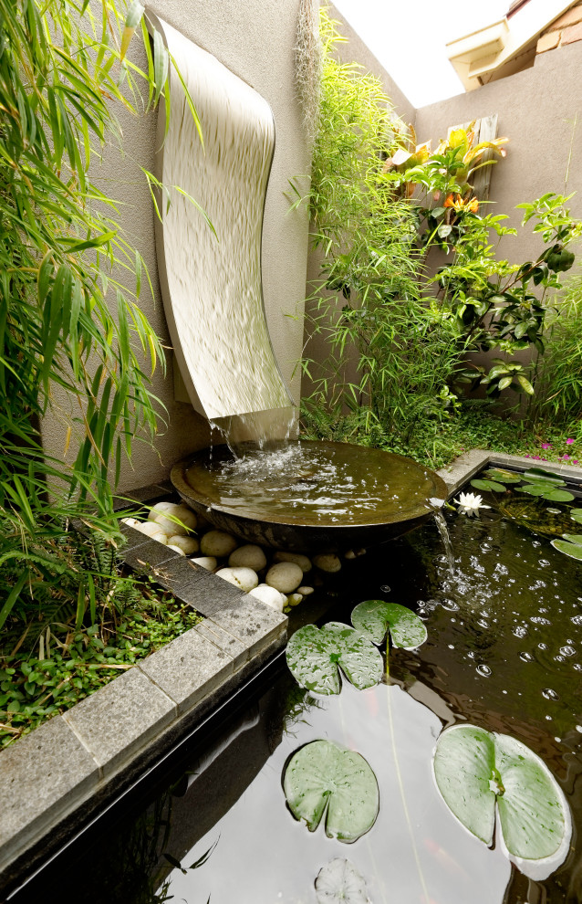 Bild på en liten tropisk trädgård i delvis sol vattenfall, med naturstensplattor