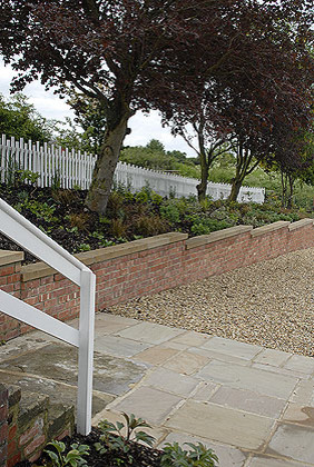 Cette photo montre un grand jardin arrière éclectique avec un mur de soutènement, une exposition ensoleillée et des pavés en pierre naturelle.