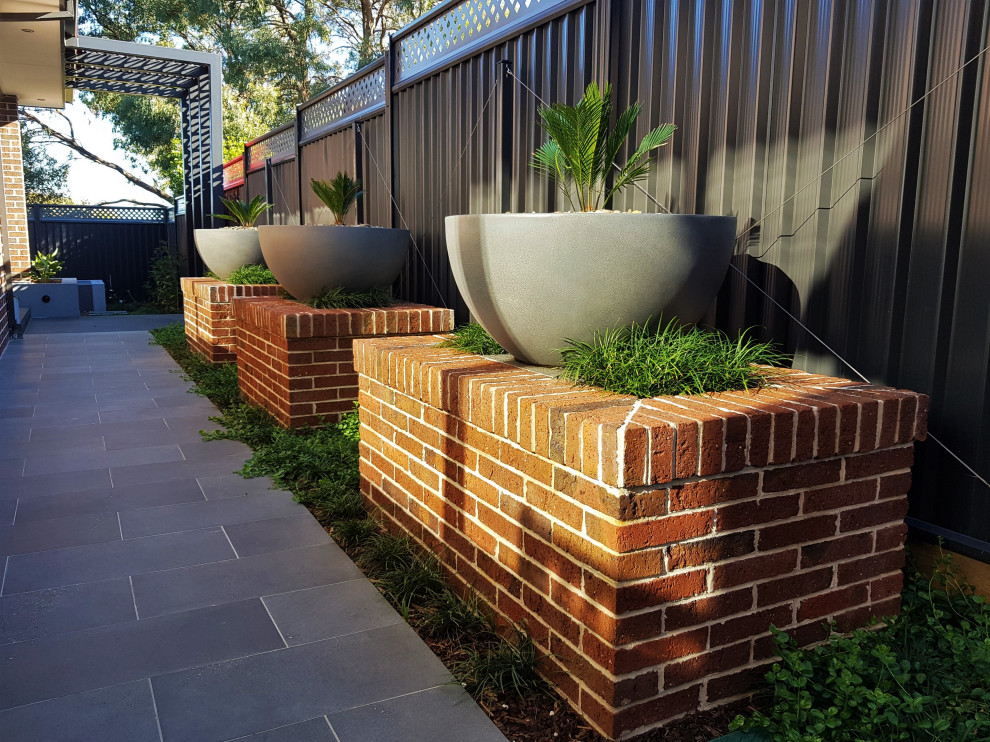 This is an example of a medium sized modern back formal partial sun garden for summer in Melbourne with a flowerbed and natural stone paving.