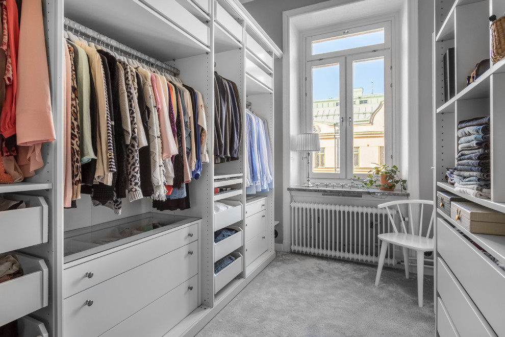 На фото: гардеробная комната среднего размера, унисекс в скандинавском стиле с открытыми фасадами, белыми фасадами, ковровым покрытием и серым полом с