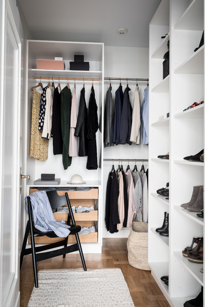 На фото: гардеробная комната унисекс в скандинавском стиле с открытыми фасадами, белыми фасадами и светлым паркетным полом с