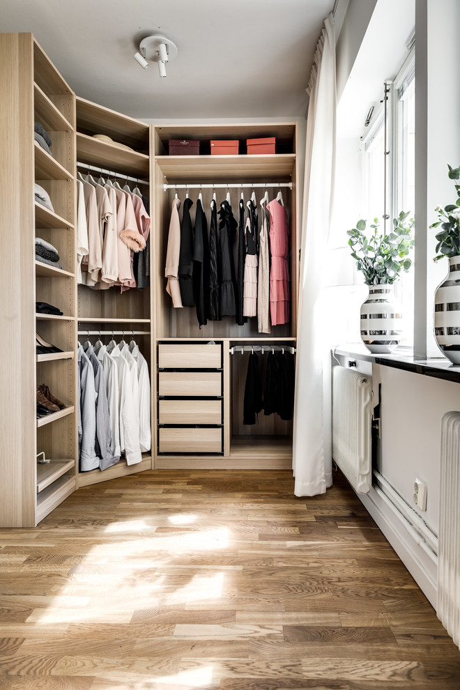 This is an example of a contemporary walk-in wardrobe for women in Stockholm with light wood cabinets, laminate floors, beige floors and feature lighting.