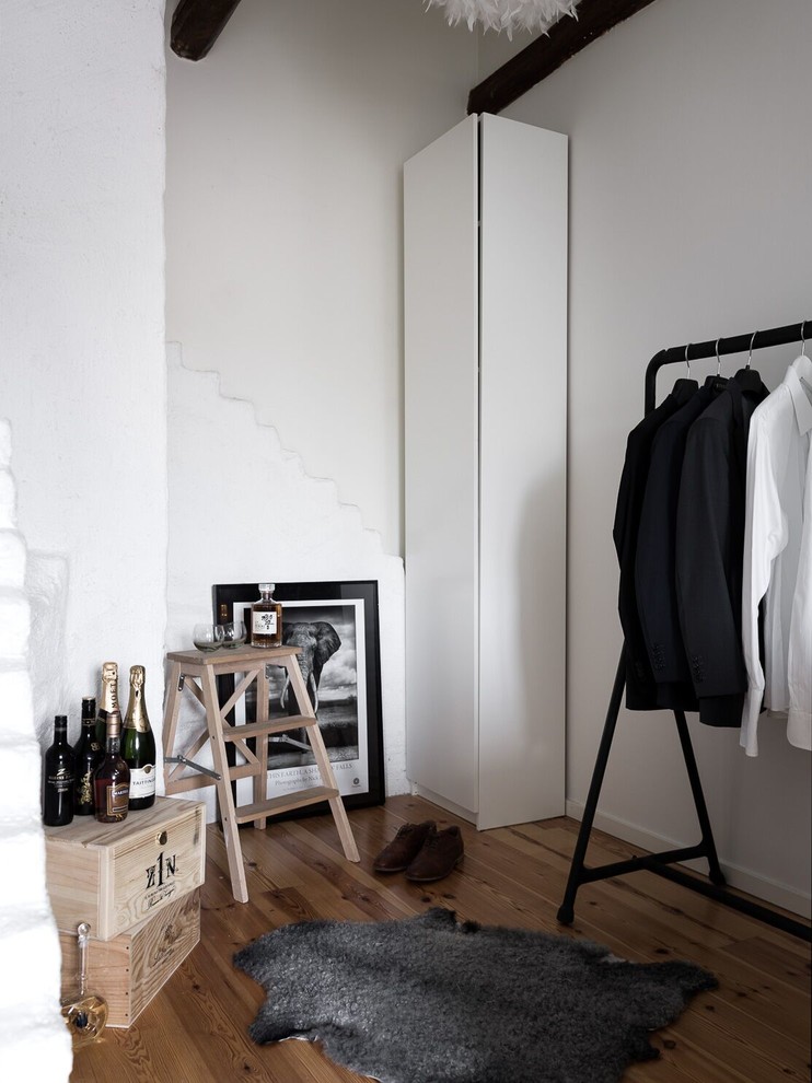 This is an example of a medium sized scandi gender neutral dressing room in Stockholm with flat-panel cabinets, white cabinets, light hardwood flooring and brown floors.