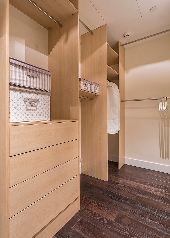 This is an example of a contemporary gender neutral walk-in wardrobe in Moscow with flat-panel cabinets, light wood cabinets and dark hardwood flooring.
