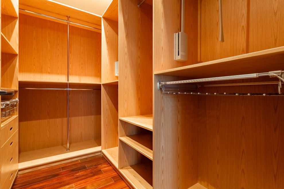 This is an example of a medium sized contemporary gender neutral walk-in wardrobe in Moscow with light wood cabinets, dark hardwood flooring and brown floors.
