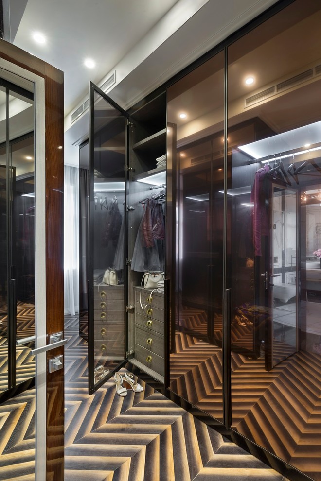 На фото: гардеробная комната унисекс в современном стиле с стеклянными фасадами и темным паркетным полом с