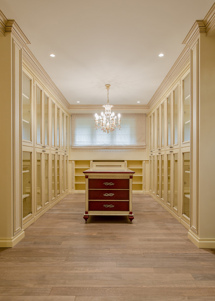 Cette image montre un dressing room traditionnel neutre avec un placard à porte vitrée, des portes de placard blanches et un sol en bois brun.