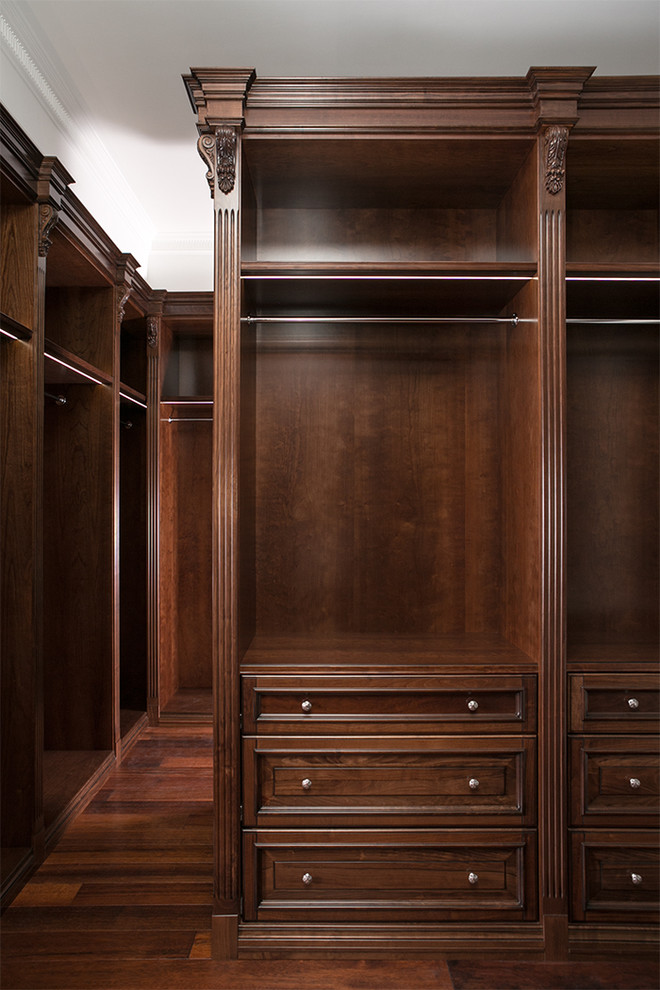 Diseño de armario vestidor unisex clásico pequeño con armarios con rebordes decorativos, puertas de armario de madera en tonos medios y suelo de madera oscura