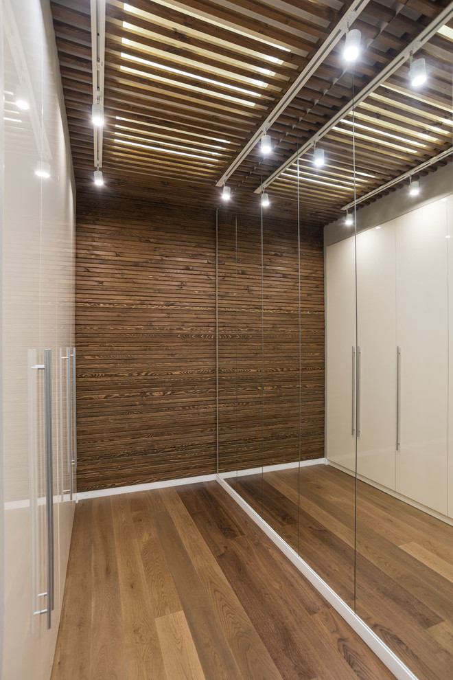 Neutrales Modernes Ankleidezimmer mit flächenbündigen Schrankfronten, weißen Schränken, braunem Holzboden und braunem Boden in Sonstige
