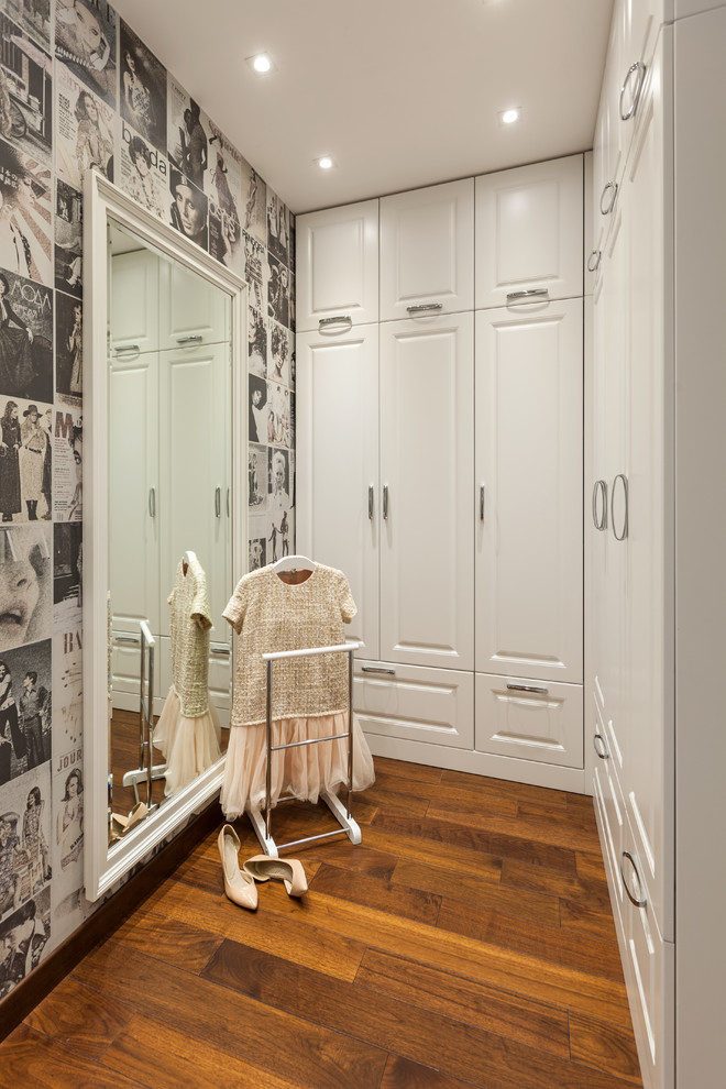 Идея дизайна: гардеробная комната в стиле неоклассика (современная классика) с белыми фасадами, паркетным полом среднего тона и коричневым полом для женщин