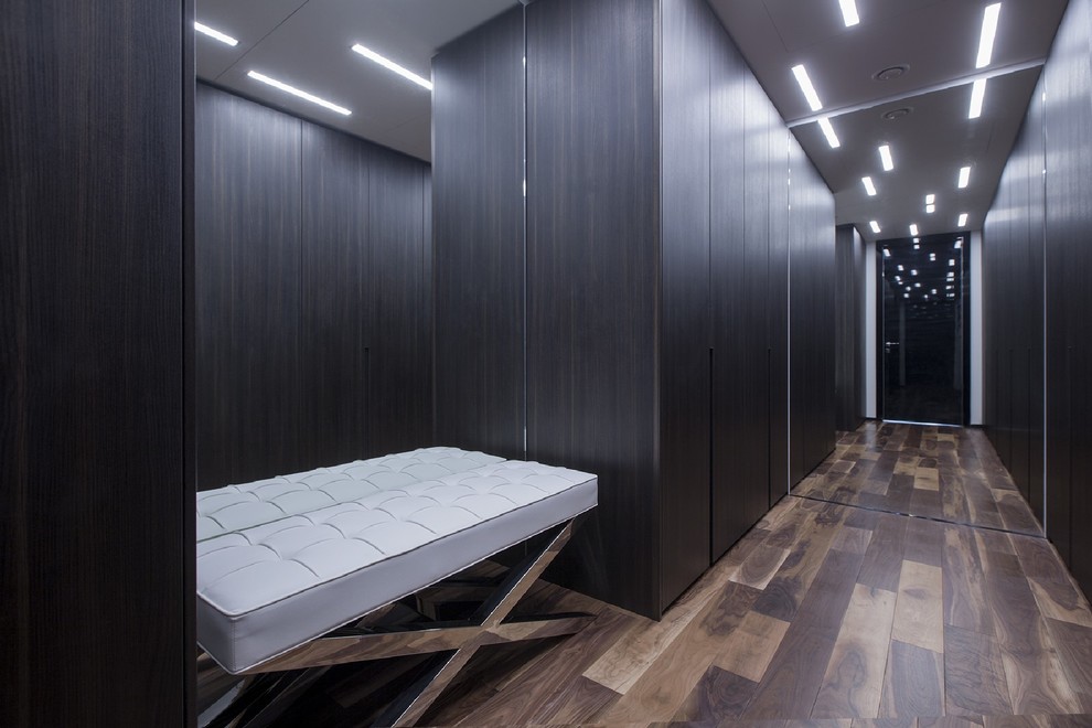 На фото: гардеробная комната унисекс в современном стиле с плоскими фасадами, темными деревянными фасадами и паркетным полом среднего тона с