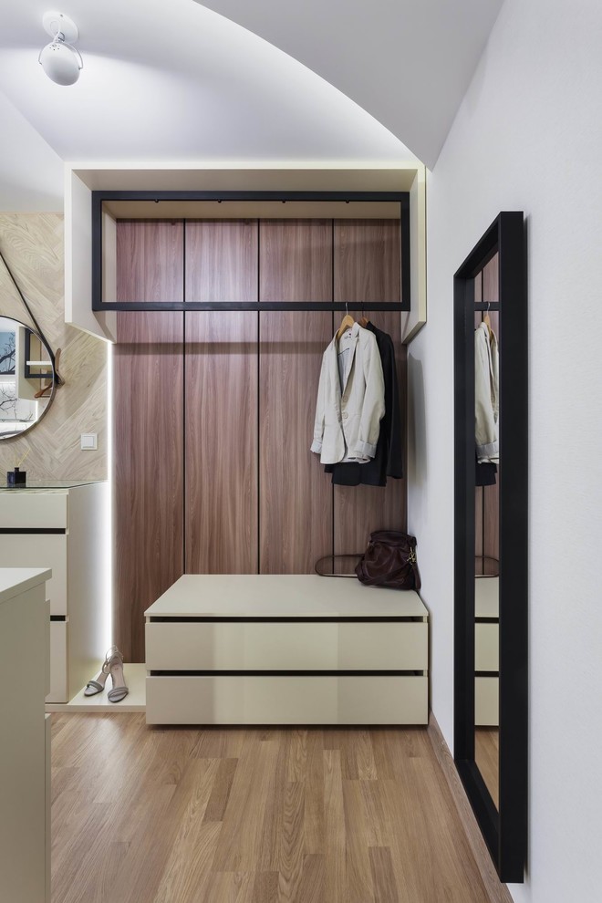 Imagen de vestidor unisex actual con armarios con paneles lisos, puertas de armario blancas, suelo de madera en tonos medios y suelo marrón