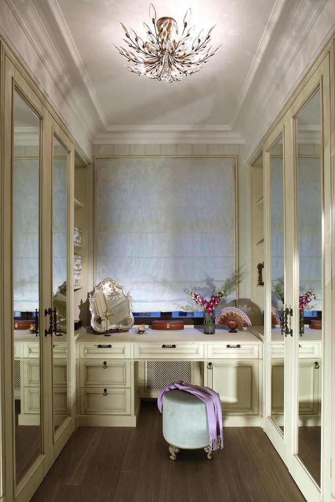 Klassisk inredning av ett omklädningsrum, med luckor med infälld panel, beige skåp, mellanmörkt trägolv och brunt golv
