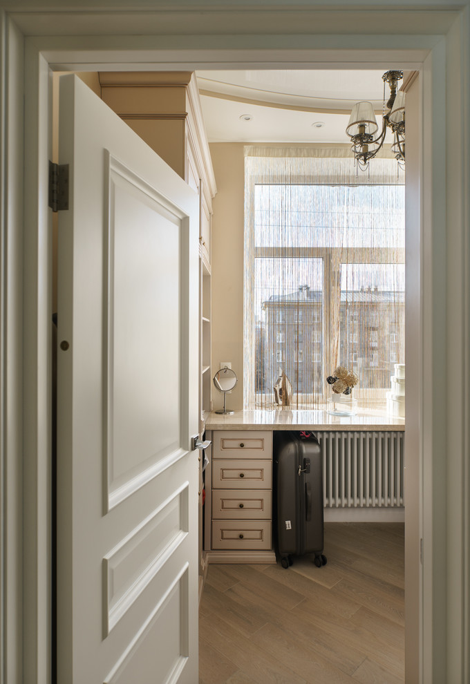 Foto de armario vestidor clásico de tamaño medio con armarios con paneles con relieve, puertas de armario de madera clara, suelo de madera clara y suelo beige