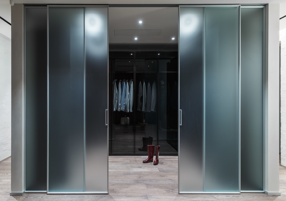Imagen de armario vestidor unisex contemporáneo grande con armarios tipo vitrina, puertas de armario negras, suelo de madera clara y suelo beige