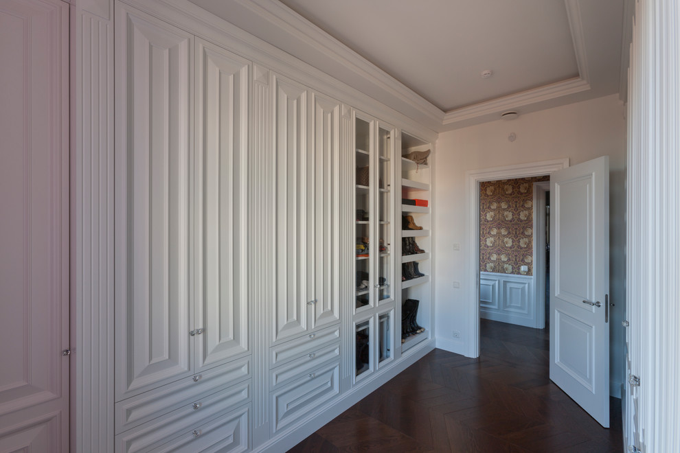 Источник вдохновения для домашнего уюта: гардеробная комната унисекс в классическом стиле с фасадами с выступающей филенкой, белыми фасадами, темным паркетным полом и коричневым полом