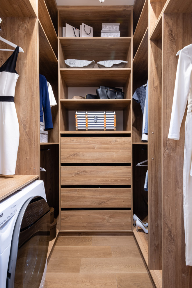 Immagine di una cabina armadio unisex design con ante lisce, ante in legno chiaro, parquet chiaro e pavimento marrone
