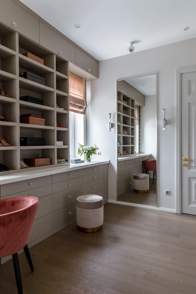 This is an example of a contemporary gender neutral dressing room in Other with flat-panel cabinets, grey cabinets, medium hardwood flooring and brown floors.