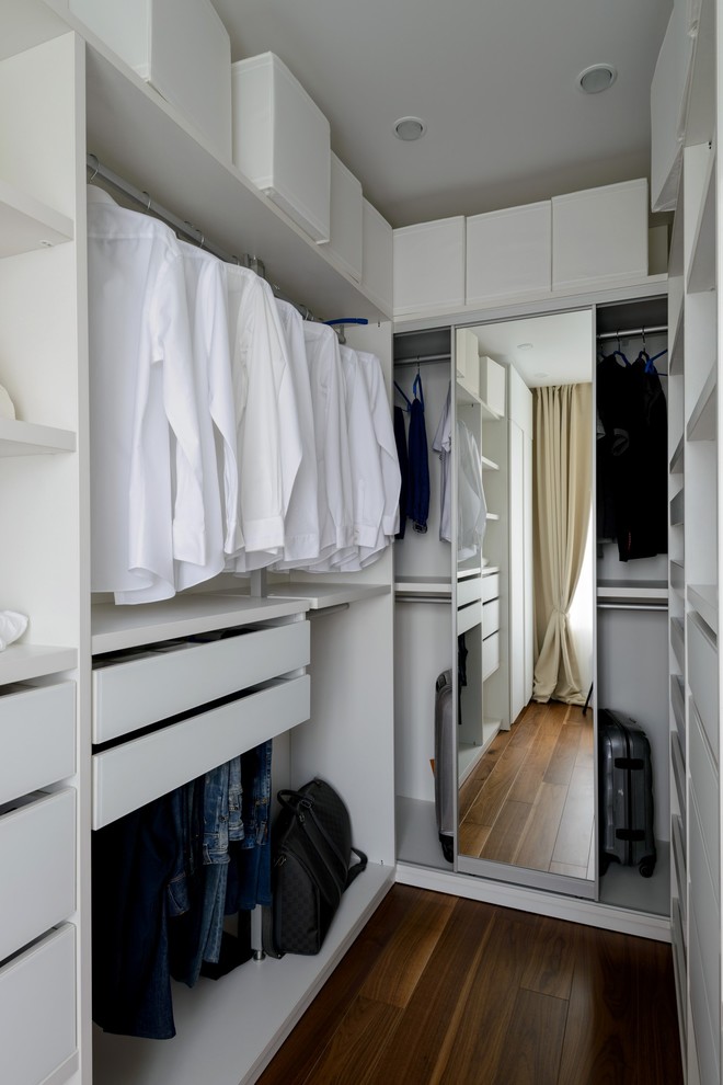 Cette photo montre un dressing tendance neutre avec un placard à porte plane, des portes de placard blanches, parquet foncé et un sol marron.