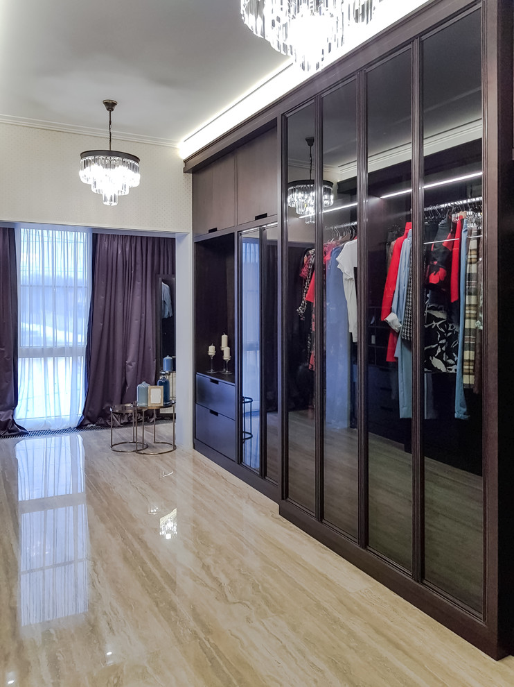 Пример оригинального дизайна: большая гардеробная комната в стиле неоклассика (современная классика) с стеклянными фасадами, темными деревянными фасадами, полом из керамогранита и бежевым полом