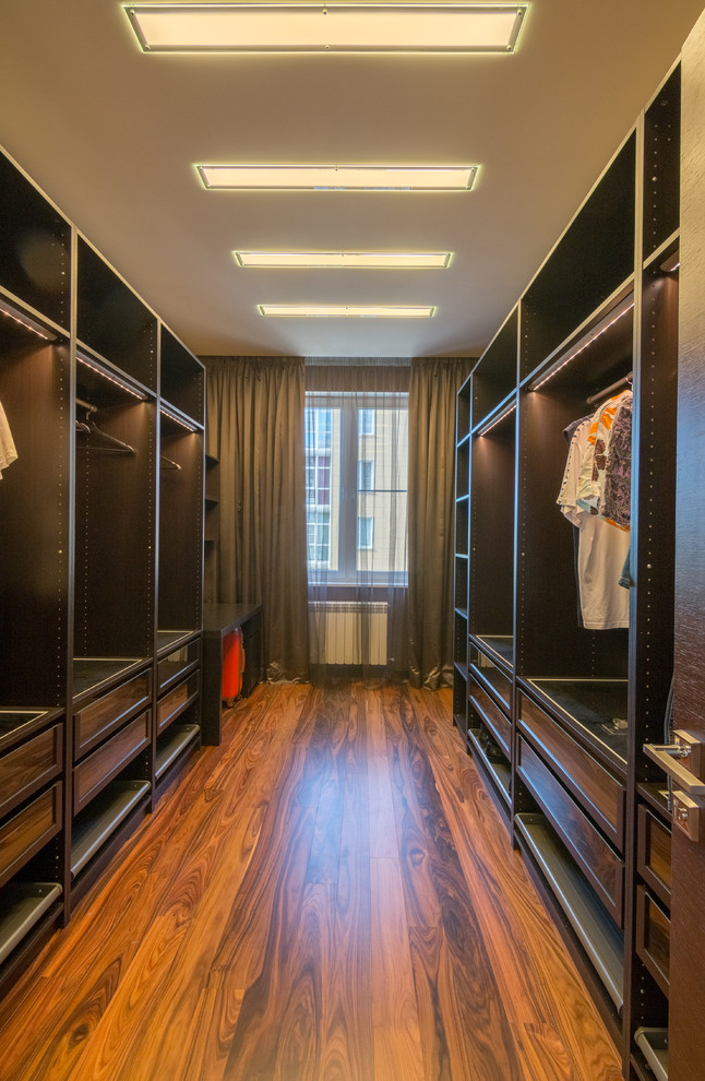 Large trendy men's medium tone wood floor walk-in closet photo in Other with dark wood cabinets