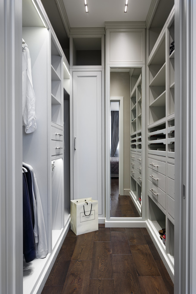 Пример оригинального дизайна: гардеробная комната унисекс в стиле неоклассика (современная классика) с фасадами с утопленной филенкой, белыми фасадами, темным паркетным полом и коричневым полом