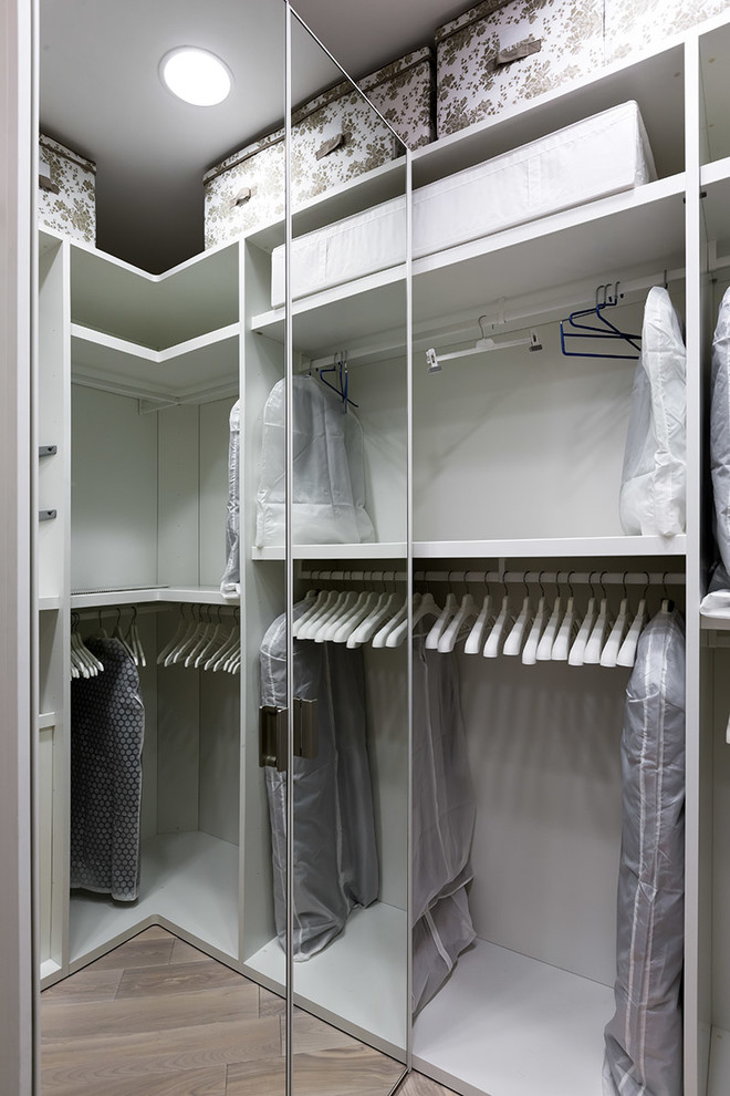 Foto di una cabina armadio unisex design di medie dimensioni con ante bianche, pavimento beige, ante lisce e parquet chiaro