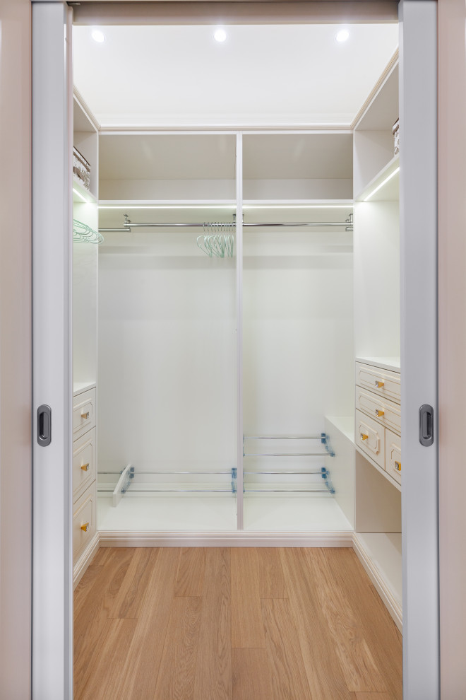 Imagen de armario y vestidor unisex clásico renovado pequeño con armarios con paneles con relieve, puertas de armario blancas, suelo de madera clara y suelo beige