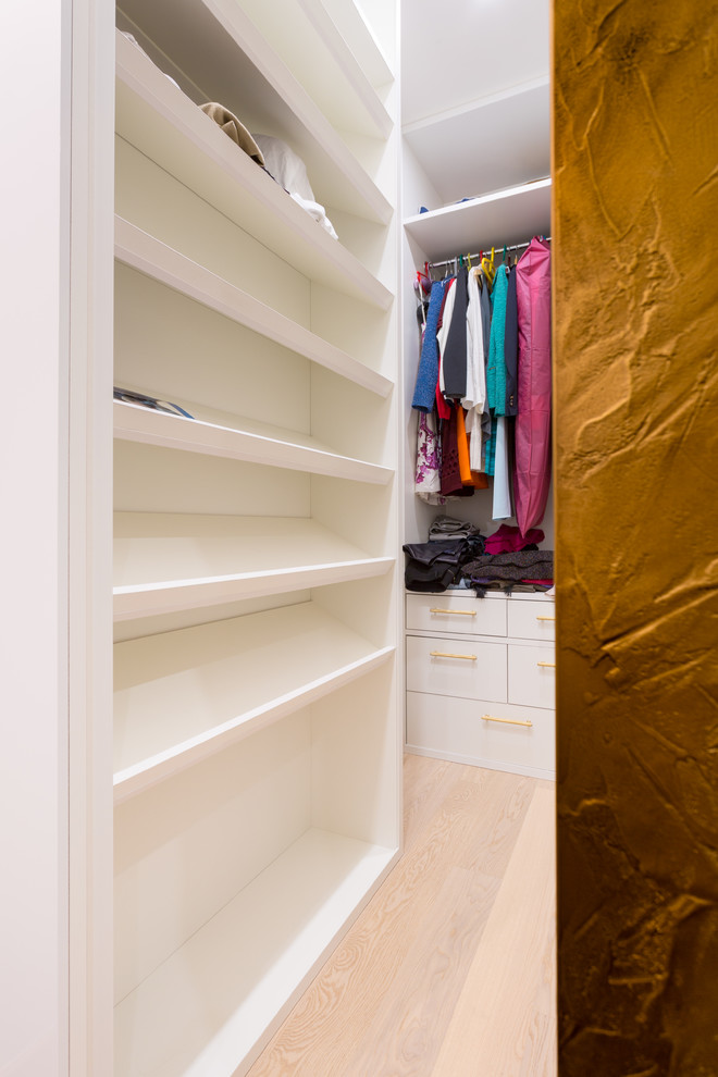 Example of a mid-sized trendy medium tone wood floor and white floor walk-in closet design in Moscow with flat-panel cabinets and white cabinets