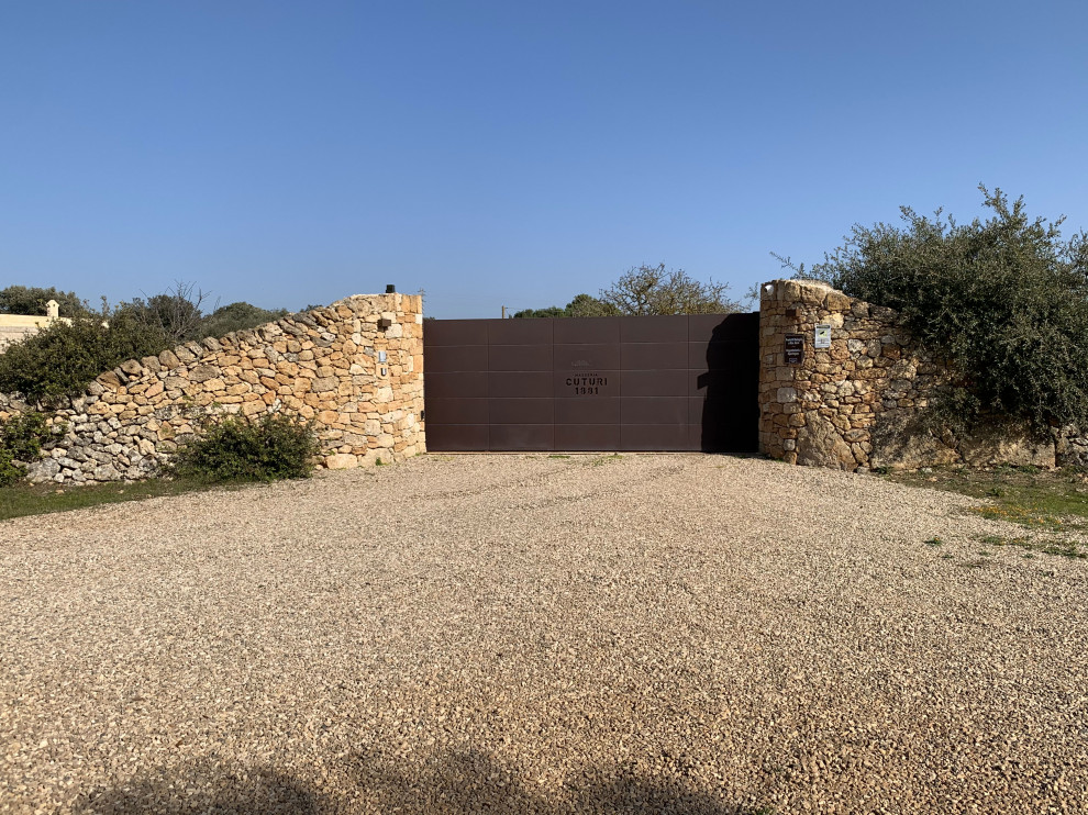 Immagine di un giardino mediterraneo con cancello, pacciame e recinzione in pietra