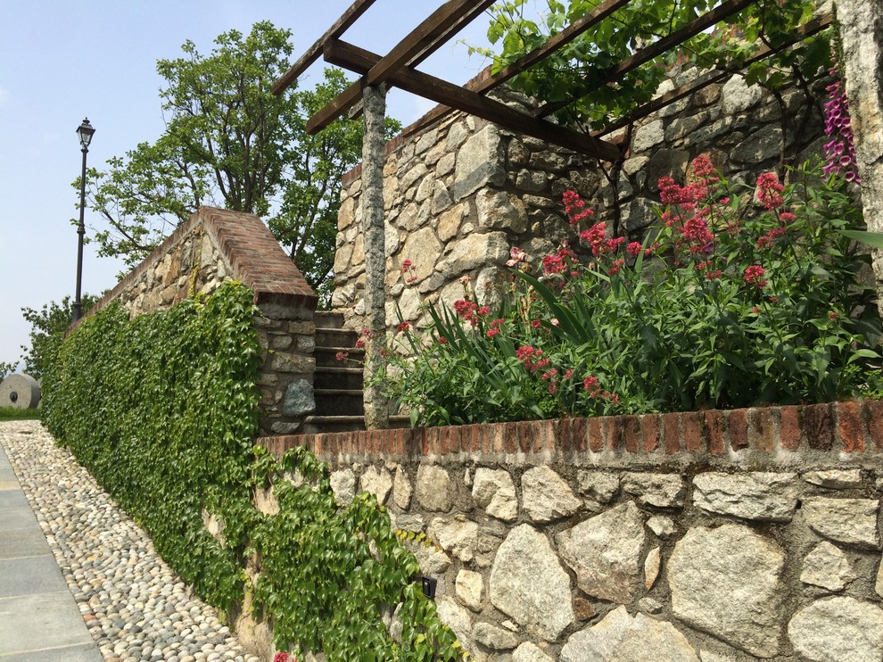 Immagine di un grande giardino country esposto in pieno sole in estate con un muro di contenimento, un pendio, una collina o una riva e pavimentazioni in pietra naturale