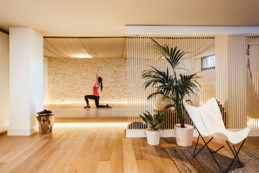 This is an example of a mediterranean home yoga studio in Barcelona with light hardwood flooring, beige walls, beige floors and a feature wall.