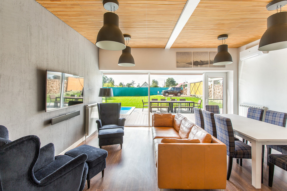 Diseño de salón para visitas abierto actual con paredes grises, suelo de madera en tonos medios y televisor colgado en la pared