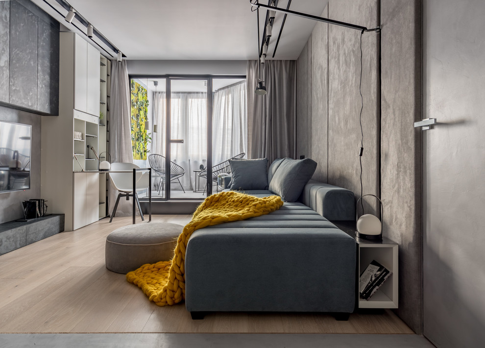 Стильный дизайн: маленькая гостиная комната в стиле лофт с серыми стенами, светлым паркетным полом, бежевым полом, телевизором на стене и тюлем на окнах для на участке и в саду - последний тренд