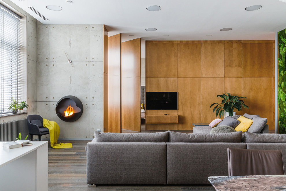Cette image montre un salon design avec un mur gris, un sol en bois brun, un téléviseur fixé au mur et un sol marron.