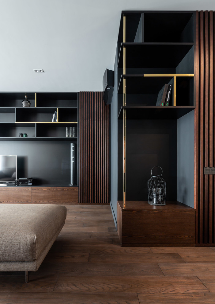 Пример оригинального дизайна: большая открытая гостиная комната в современном стиле с с книжными шкафами и полками, разноцветными стенами, паркетным полом среднего тона, мультимедийным центром и коричневым полом без камина
