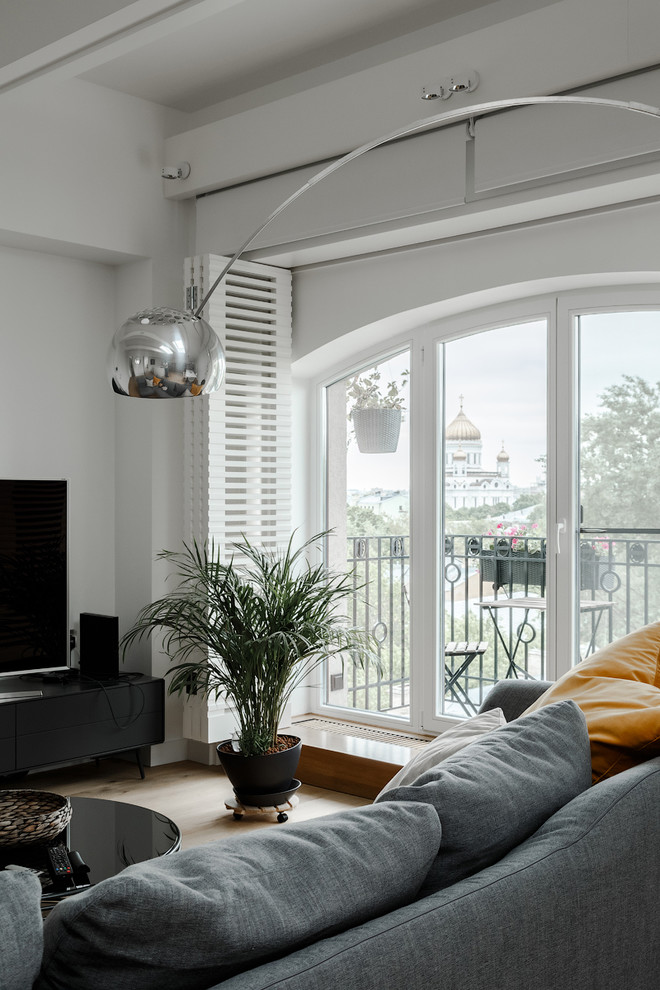 Пример оригинального дизайна: гостиная комната в стиле неоклассика (современная классика) с белыми стенами, светлым паркетным полом и отдельно стоящим телевизором